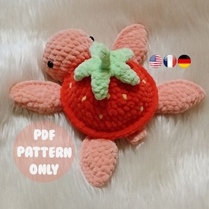 Puede incluir: Un juguete amigurumi de tortuga fresa tejido a crochet con una hoja verde en la parte superior. El juguete es rosa y rojo con ojos negros. El texto "PDF PATTERN ONLY" es visible en la imagen.