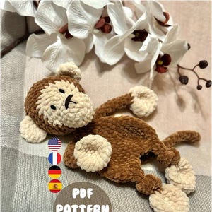 May include: A crocheted monkey toy with brown fur and cream-colored hands and feet. The toy is lying on a plaid blanket with the text "PDF PATTERN ONLY" in a circle.