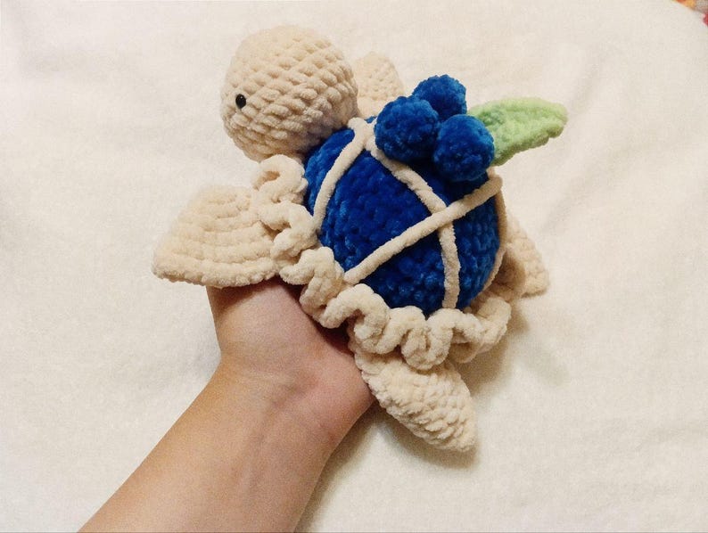 May include: A crocheted turtle toy with a blue shell and a green leaf. The shell is decorated with blue yarn balls.
