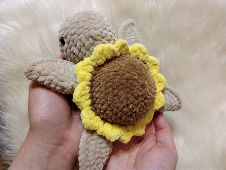 May include: A crocheted stuffed turtle toy with a brown shell and a yellow sunflower design.