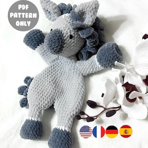 May include: A handmade crochet unicorn plushie in shades of gray and blue. The stuffed animal has a fluffy mane, ears, and tail. The image includes the text "PDF PATTERN ONLY" in a circular graphic.