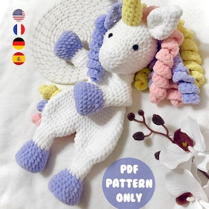 May include: A handmade white crochet unicorn with a yellow horn, and multi-colored mane and tail. The unicorn has blue, pink, and yellow accents. The text "PDF PATTERN ONLY" is in a blue circle.