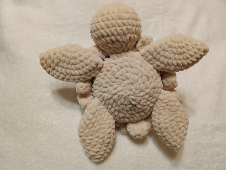 May include: A crocheted plush toy shaped like a turtle. The turtle is beige and has a textured surface. The turtle is lying on its back with its legs and head visible.