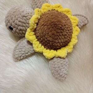 May include: A crocheted turtle toy with a brown shell and a yellow sunflower design. The turtle is made with soft, fuzzy yarn and has a sweet, friendly expression.
