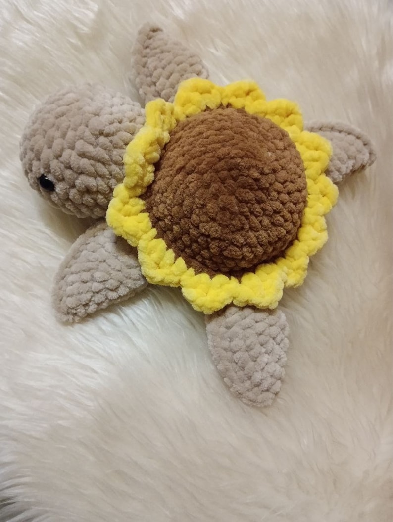 May include: A crocheted turtle toy with a brown shell and a yellow sunflower design. The turtle is made with soft, fuzzy yarn and has a sweet, friendly expression.