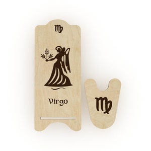 May include: Wooden phone stand with a Virgo zodiac sign and the symbol "♍" engraved on it. The stand has a cutout for holding a phone.