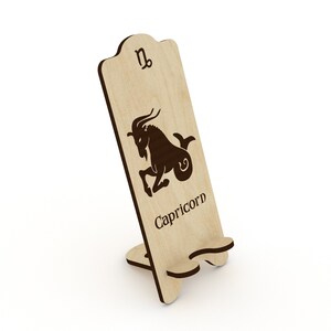 May include: Wooden phone stand with a cutout of the Capricorn zodiac sign and the word "Capricorn" below it.