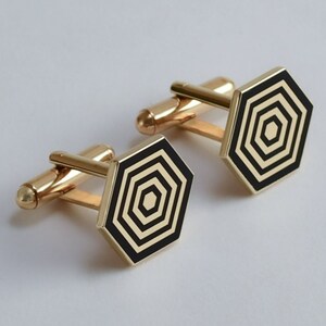 May include: A pair of gold cufflinks with black hexagonal designs. Each cufflink features a concentric circle pattern.
