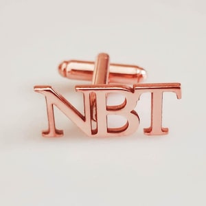 以下が含まれることがあります： 「NBT」という文字が刻まれた、ローズゴールドのカフスボタンです。