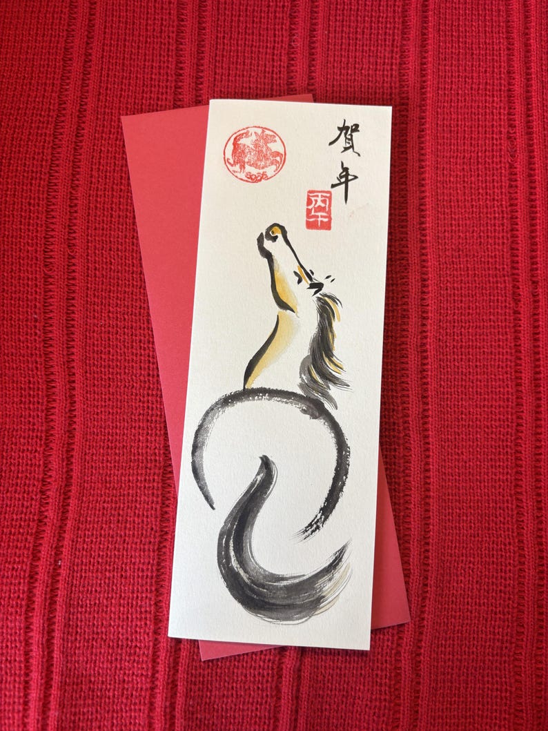 K&ouml;nnte beinhalten: Eine Gru&szlig;karte mit einer Aquarellillustration eines Pferdes in Schwarz, Gelb und Wei&szlig;, mit japanischer Kalligraphie und einem roten Siegel. Die Karte liegt auf rotem Hintergrund, mit einem roten Umschlag.