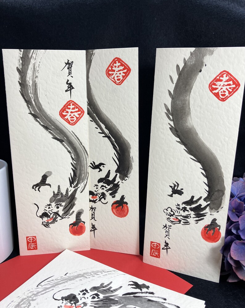 Puede incluir: Tres pinturas de dragones de tinta negra sobre papel blanco con caracteres chinos rojos y un sello rojo. Los caracteres en la pintura m&aacute;s a la izquierda dicen "A&ntilde;o Nuevo Chino". Los caracteres en la pintura del medio dicen "Primavera". Los caracteres en la pintura m&aacute;s a la derecha dicen "Primavera".