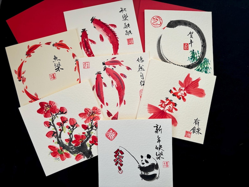 K&ouml;nnte beinhalten: Eine Sammlung quadratischer Gru&szlig;karten mit Illustrationen in roter und schwarzer Tinte. Die Karten zeigen Kois, Blumen und einen Panda. Rote Umschl&auml;ge sind sichtbar. Einige Karten haben chinesische Schriftzeichen.