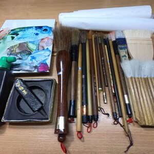Może przedstawiać: Zestaw do kaligrafii, w skład kt&oacute;rego wchodzi butelka czarnego atramentu, kamień do atramentu, czarny pręt atramentowy, paleta akwarelowa i r&oacute;żne pędzle. Pędzle są wykonane z naturalnego włosia i mają drewniane uchwyty.