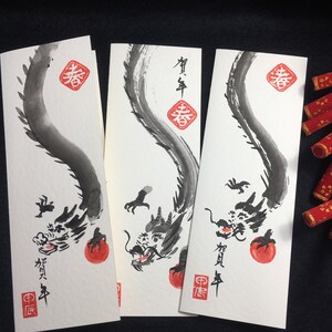 Puede incluir: Tres tarjetas blancas con dibujos de dragones en tinta negra que sostienen esferas rojas. Las tarjetas tienen caracteres chinos en tinta roja. Los caracteres en las tarjetas son "Primavera" y "Feliz A&ntilde;o Nuevo".