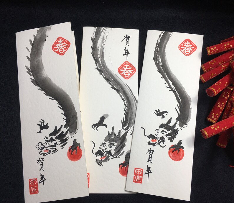 Puede incluir: Tres tarjetas blancas con dibujos de dragones en tinta negra que sostienen esferas rojas. Las tarjetas tienen caracteres chinos en tinta roja. Los caracteres en las tarjetas son "Primavera" y "Feliz A&ntilde;o Nuevo".