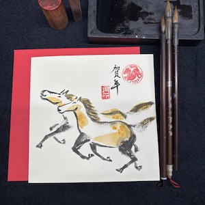 May include: An artistic composition featuring a watercolor painting of two running horses, accompanied by calligraphy brushes, ink, a stone ink well, and two wooden stamps. The painting has a red border.