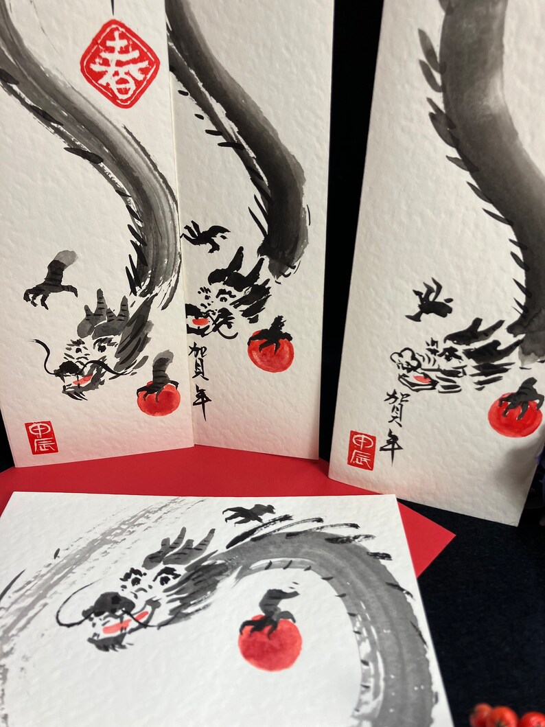Puede incluir: Tres pinturas de tinta negra de un drag&oacute;n con un c&iacute;rculo rojo en su boca. El drag&oacute;n est&aacute; enroscado alrededor del c&iacute;rculo. Las pinturas est&aacute;n sobre papel blanco con caracteres chinos rojos. Los caracteres en la pintura m&aacute;s a la izquierda son "中庸". Los caracteres en la pintura del medio son "新年". Los caracteres en la pintura m&aacute;s a la derecha son "新年".