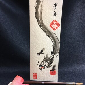 Puede incluir: Una pintura de tinta negra de un drag&oacute;n sobre un fondo blanco. El drag&oacute;n est&aacute; enroscado y tiene un orbe rojo en su boca. La pintura est&aacute; firmada en caracteres chinos y tiene un sello rojo.