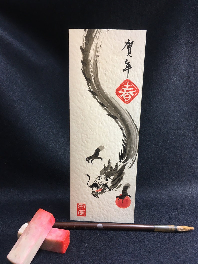 Puede incluir: Una pintura de tinta negra de un drag&oacute;n sobre un fondo blanco. El drag&oacute;n est&aacute; enroscado y tiene un orbe rojo en su boca. La pintura est&aacute; firmada en caracteres chinos y tiene un sello rojo.