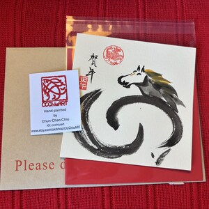 Pode incluir: Uma impress&atilde;o de arte com uma ilustra&ccedil;&atilde;o de cavalo a preto e branco e caligrafia. A impress&atilde;o est&aacute; num cart&atilde;o branco com detalhes em vermelho, acompanhada por um cart&atilde;o de visita e um envelope castanho. O fundo &eacute; tecido vermelho.