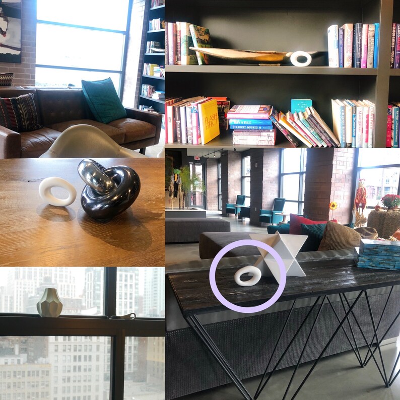 May include: A small, smooth, white oval-shaped decorative object with a hollow center. The object is shown in various settings, including on a wooden table, on a bookshelf, on a window sill, and on a dark console table next to a white geometric star.