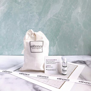 May include: A beige drawstring cotton pouch with the black text "escence Home Fragrance" printed on the front, accompanied by a small white instruction card and a clear glass dropper bottle with a white cap and "escence" label.