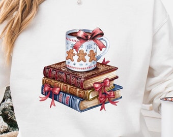 May include: White sweatshirt featuring a design of a mug of hot chocolate with marshmallows and a red bow, sitting on top of a stack of books with red bows.