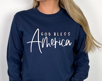 May include: Navy blue long-sleeved shirt with white text that reads "God Bless America" in a cursive font.