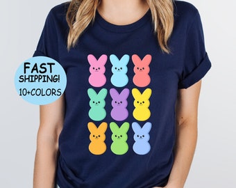 Könnte beinhalten: Marineblaues T-Shirt mit einem bunten Hasendesign. Die Hasen sind in einem Raster angeordnet und alle lächeln. Das Shirt hat einen Rundhalsausschnitt und kurze Ärmel.