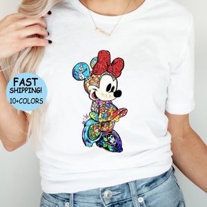May include: White t-shirt featuring a colorful graphic of Minnie Mouse with a red bow. The graphic is filled with various Disney characters. Text on the shirt reads "FAST SHIPPING! 10+ COLORS".