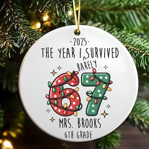 May include: White ceramic Christmas ornament with gold hanging ribbon. The ornament features the text "-2025- THE YEAR I SURVIVED BARELY" and the numbers "67" decorated with Christmas lights. Below the numbers is "MRS. BROOKS 6TH GRADE".