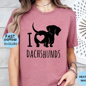 May include: A heather mauve t-shirt with a black silhouette of a dachshund with a heart on its back and the text "I love dachshunds".