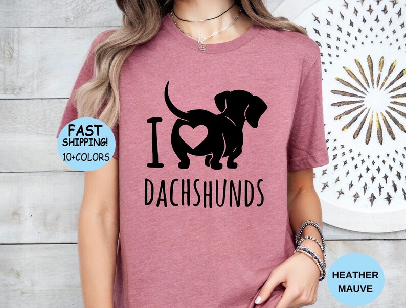 May include: A heather mauve t-shirt with a black silhouette of a dachshund with a heart on its back and the text "I love dachshunds".