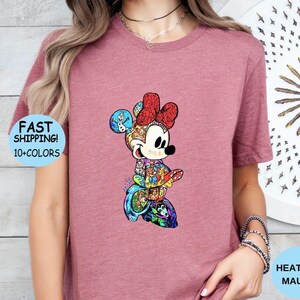 May include: Heather mauve t-shirt featuring a colorful Minnie Mouse graphic. The Minnie Mouse design is composed of various cartoon characters and has a red bow. The shirt also has the text "FAST SHIPPING! 10+ COLORS".