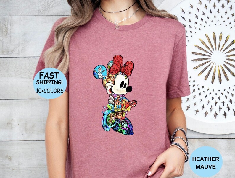 May include: Heather mauve t-shirt featuring a colorful Minnie Mouse graphic. The Minnie Mouse design is composed of various cartoon characters and has a red bow. The shirt also has the text "FAST SHIPPING! 10+ COLORS".