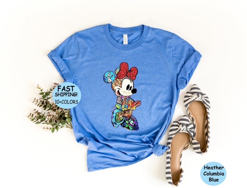 May include: Heather Columbia Blue t-shirt featuring a colorful Minnie Mouse design. The graphic is composed of various Disney characters and elements. The shirt has rolled-up sleeves and the text "FAST SHIPPING! 10+COLORS" is visible.