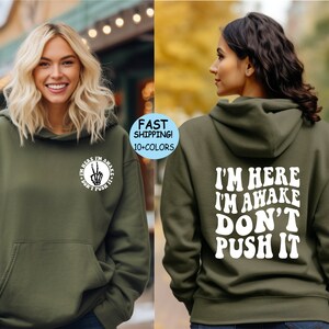 May include: A green hooded sweatshirt with the text "I'm here I'm awake Don't push it" printed in white on the back. The front of the sweatshirt has a small circle with a peace sign and the text "I'm here I'm awake Don't push it" printed in white.