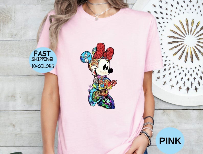 May include: A light pink t-shirt featuring a colorful Minnie Mouse design. The Minnie Mouse graphic is detailed with various patterns and colors. The shirt also has the text "FAST SHIPPING! 10+ COLORS" in a blue circle and the word "PINK" in a blue circle.