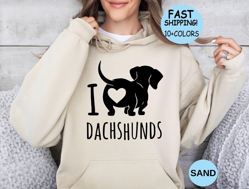 May include: A beige hoodie with a black graphic of a dachshund with a heart on its rear end. The text "I love dachshunds" is printed below the graphic.