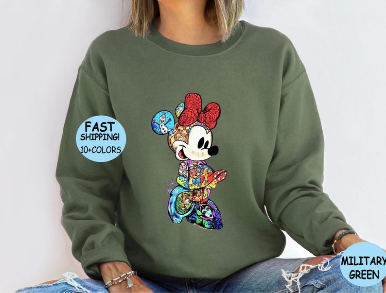 May include: Olive green sweatshirt featuring a colorful Minnie Mouse graphic. The Minnie Mouse design includes a red bow, and various character illustrations. The sweatshirt has the text "FAST SHIPPING! 10+ COLORS" on the left side and "MILITARY GREEN" on the right side.