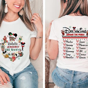 May include: White t-shirt with a Christmas-themed design featuring Mickey Mouse and friends drinking around the world. The text "Drinking Around the World" is printed on the shirt. The back of the shirt has a list of countries with the text "Drinking Around the World" at the top.