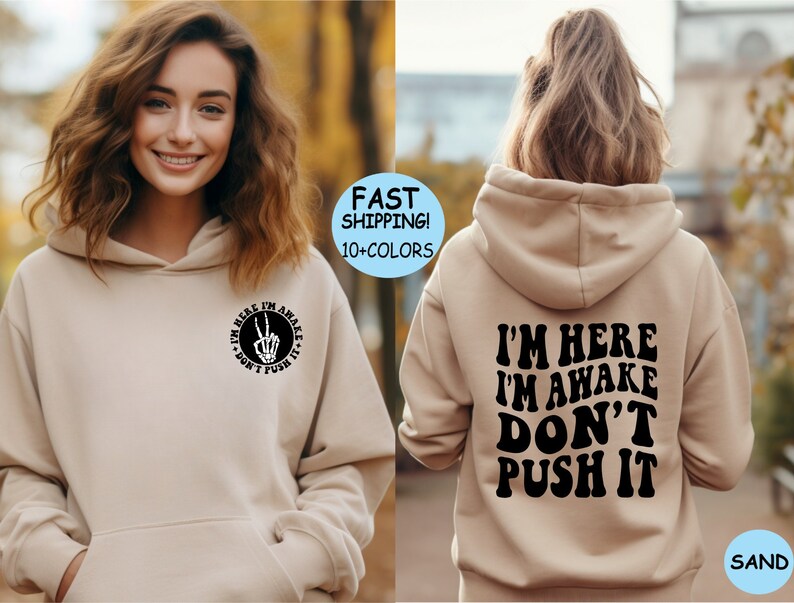 May include: A sand-colored hoodie with a black graphic on the front that says "I'm here I'm awake don't push it" with a peace sign and skeleton hand. The back of the hoodie has the same text in a larger font.
