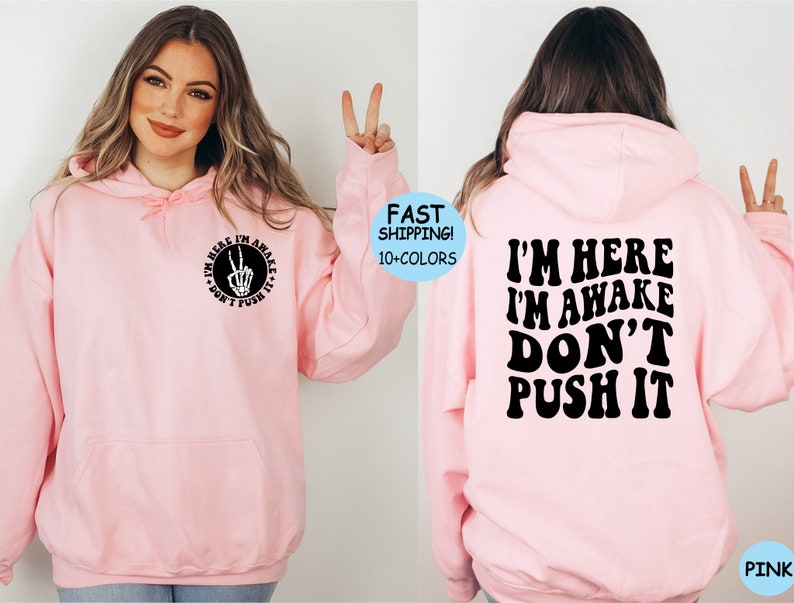 May include: Pink hoodie with a black graphic on the front that says "I'm here I'm awake don't push it" with a peace sign and skeleton hand. The back of the hoodie has the same text in a larger font.