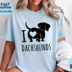 May include: A light blue t-shirt with a black dachshund silhouette and the text "I love dachshunds".