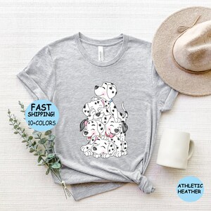 Puede incluir: Camiseta gris claro con una ilustraci&oacute;n de dibujos animados de cachorros d&aacute;lmatas. Los cachorros tienen manchas negras y est&aacute;n apilados uno encima del otro. La camiseta tiene el texto "FAST SHIPPING! 10+ COLORS" y "ATHLETIC HEATHER".