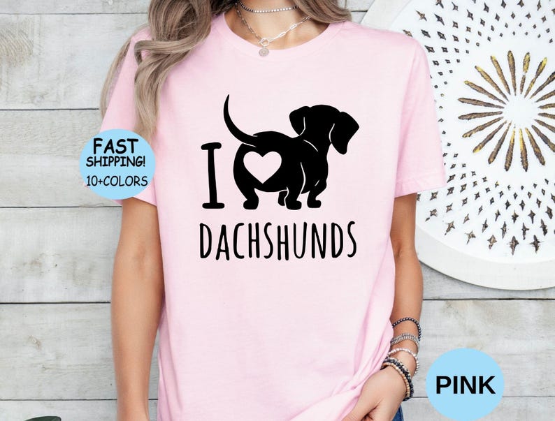May include: Pink t-shirt with a black silhouette of a dachshund with a heart in its rear end and the text "I love dachshunds".