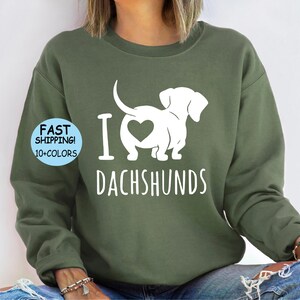 May include: A green sweatshirt with a white graphic of a dachshund with a heart on its back and the text "I love dachshunds".
