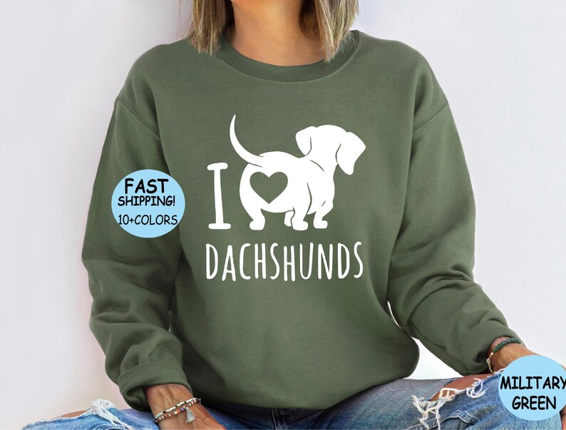 May include: A green sweatshirt with a white graphic of a dachshund with a heart on its back and the text "I love dachshunds".