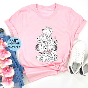 Puede incluir: Camiseta rosa con un gr&aacute;fico de cachorros d&aacute;lmatas apilados. Los cachorros son blancos y negros con caras sonrientes. La camiseta tiene las mangas enrolladas y el texto "FAST SHIPPING! 10+ COLORS".