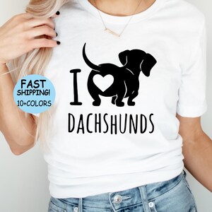May include: White t-shirt with a black silhouette of a dachshund with a heart in its rear end. The text "I love dachshunds" is printed below the dog.
